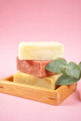 Natural handmade organic soap bars stack on wooden tray with euacalyptus leaves. Close up against a pink background. Vertical with copy space.