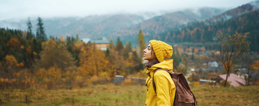 Panoramic banner image adventure woman in yellow wear with backpack standing in front beautiful mountains view, hiker girl confident looking far away