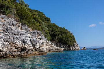 Fototapeta premium Blue sunny Ionian Sea with scenic green rocky cliffs coast and bright sky. Nature of Lefkada island in Greece. Summer vacation idyllic Ormos Desimi travel destination