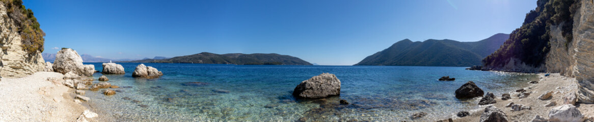 Wide panorama of white pebbles and rocks beach with azure clear water on coast of Lefkada island in Greece. Summer nature travel to Ionian Sea