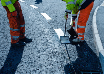 Roadworker applying thermoplastic road marking on the freshly laid tarmac during new roundabout and...