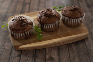 Chocolate muffins on a wooden board with green decoration, side view