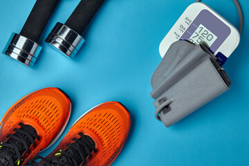 Orange sneakers, dumbbells and blood pressure monitor on a blue background