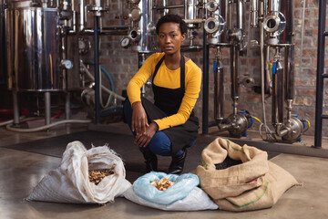 Portrait of african american woman wearing apron sitting near sacks of ingredients at gin distillery
