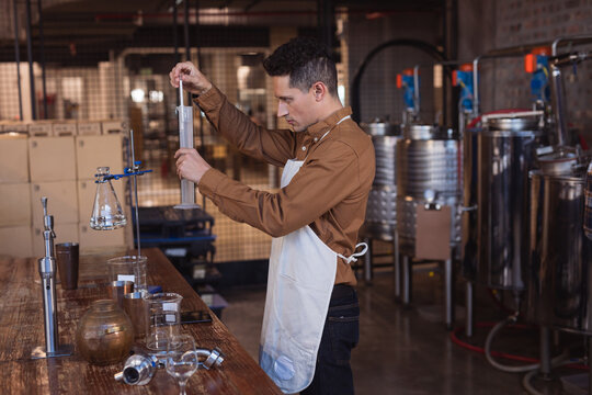Caucasian man wearing an apron checking gin product in flask at gin distillery