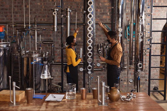 Diverse man and woman wearing face masks checking equipment at gin distillery - Powered by Adobe