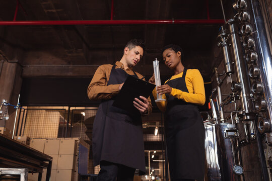 Caucasian man and african american woman checking gin product in flask at gin distillery