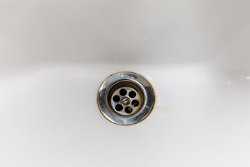 the drain hole of a white enameled bathroom with traces of dirt and rust
