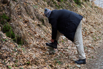 A slender man in work clothes is tying his shoe.