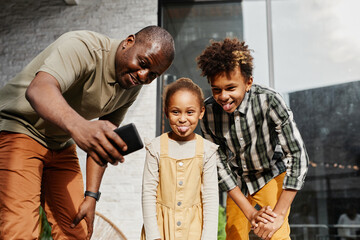 Portrait of smiling African-American man taking funny selfie with two kids outdoors