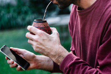 Man drinking a Mate and holding a cell phone in the hand. Yerba Mate of South America.