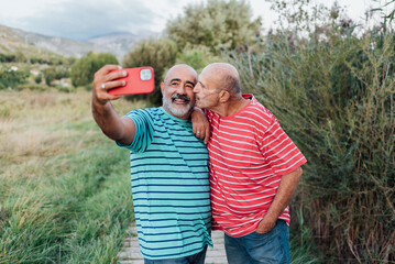 Lovely gay couple taking selfies with a mobile phone while enjoying an outdoor date in nature. LGBT...