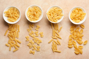 Bowls with different types of uncooked pasta on color background