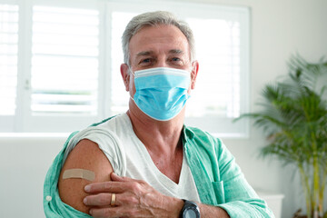 Smiling caucasian senior man with plaster on arm after vaccination, wearing face mask