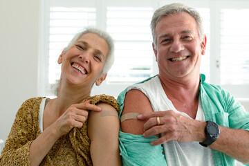 Smiling caucasian senior couple with plasters on arms after receiving vaccination, looking at camera