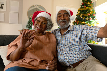 Happy african american couple wearing santa hats having video call at christmas time