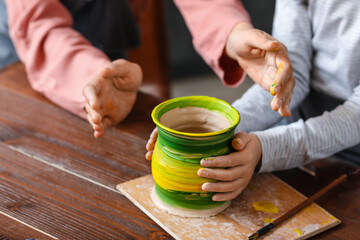 Little girl with her mother painting pot at home, closeup