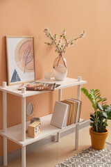 Vase with blossoming branches on shelf near color wall