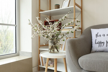 Vase with blossoming branches and book shelf in interior of modern room