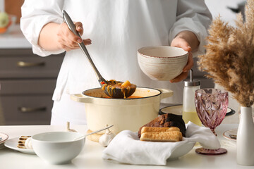 Woman pouring delicious borscht from cooking pot to bowl in kitchen, closeup
