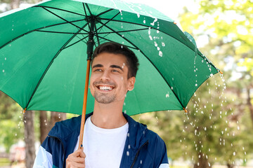 Handsome young man with umbrella in park on rainy day