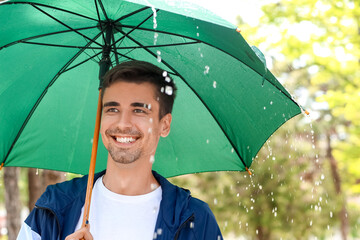 Handsome young man with umbrella in park on rainy day