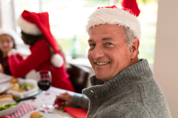 Happy senior caucasian man wearing santa hat looking at camera at christmas table