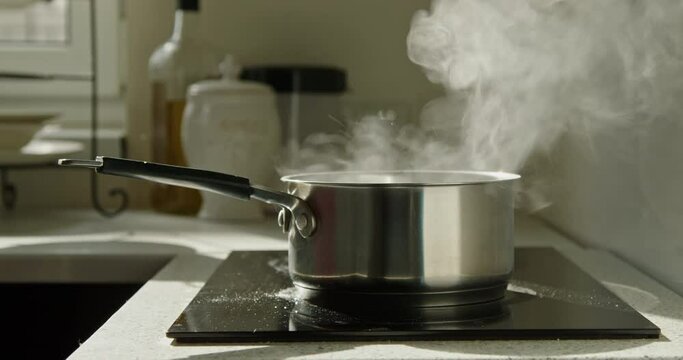 Close-up of boiling water with steam in a pot on an electric stove in the domestic kitchen