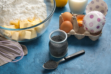 Jar with poppy seeds and ingredients for delicious muffins on color table