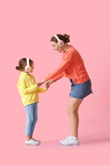 Young woman and her little daughter dancing and listening to music on color background