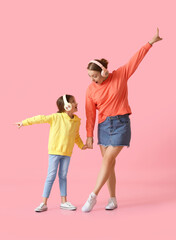 Obraz premium Young woman and her little daughter dancing and listening to music on color background