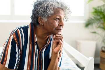 Portrait of thoughtful african american senior woman sitting on bed and look into distance - Powered by Adobe