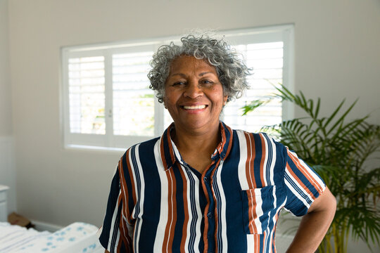 Happy african american senior woman standing in bedroom and looking at camera