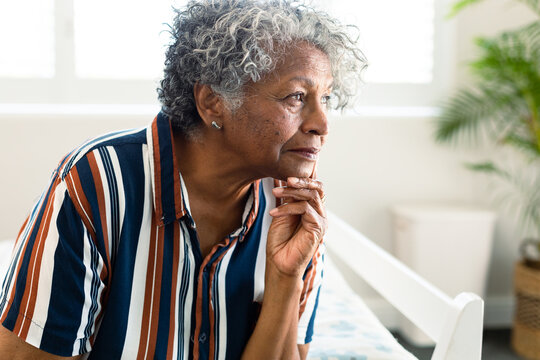 Portrait of thoughtful african american senior woman sitting on bed and look into distance