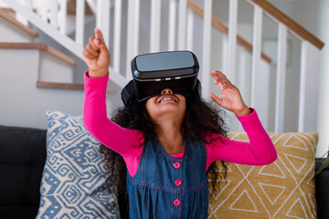Happy african american girl sitting on sofa, using vr headset and having fun