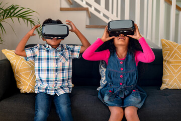 Happy african american siblings sitting on sofa, using vr headset and having fun