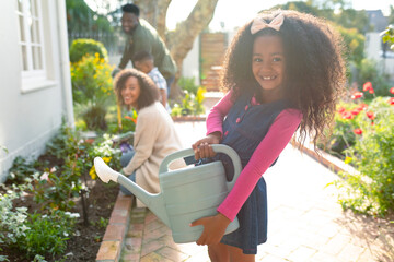 Happy african american girl and her family gardening and watering plants together