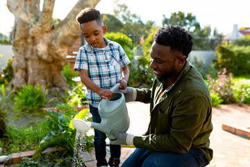 Happy african american father and son watering plants together