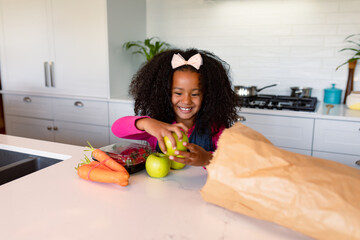Happy african american girl unpacking groceries in kitchen - obrazy, fototapety, plakaty