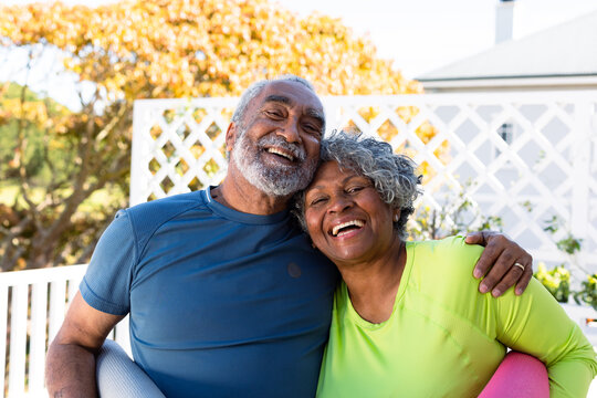 Smiling african american senior couple holding yoga mats in garden and looking at camera