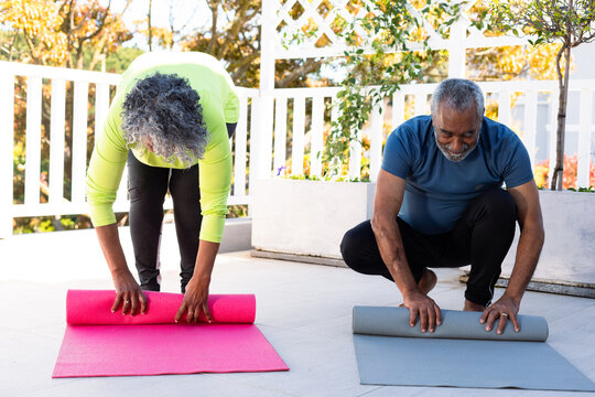 Smiling african american senior couple rolling yoga mats in garden