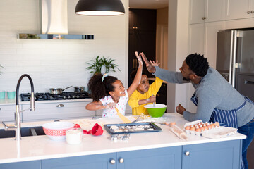 Happy african american father and siblings baking together in kitchen, giving high five