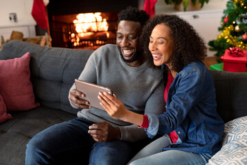 Happy african american couple having video call on tablet, christmas decorations in background - Powered by Adobe