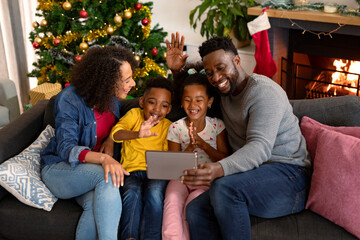 Happy african american family having video call on tablet, christmas decorations in background