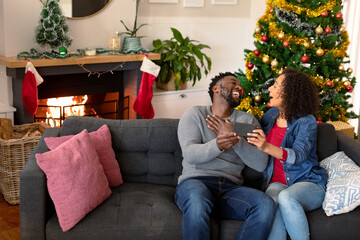 Happy african american couple having video call on smartphone, christmas decorations in background