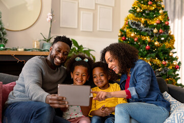 Happy african american family having video call on tablet, christmas decorations in background
