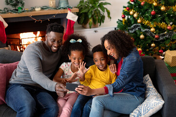 Happy african american family having video call on smartphone, christmas decorations in background