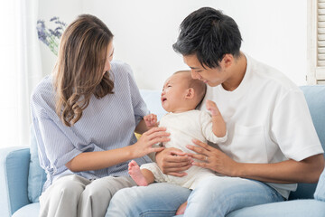 ぐずる赤ちゃんとあやすパパママ（育児・子育て・家族・ファミリー）