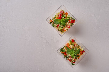 Obraz na płótnie Canvas Tabbouleh salad flat lay. Traditional Middle Eastern dish with parsley, mint, bulgur, tomatoes in transparent buffet shape cup on white background. Copy space