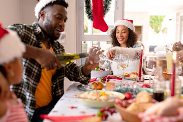 Happy african american father pouring wine to glass at christmas table